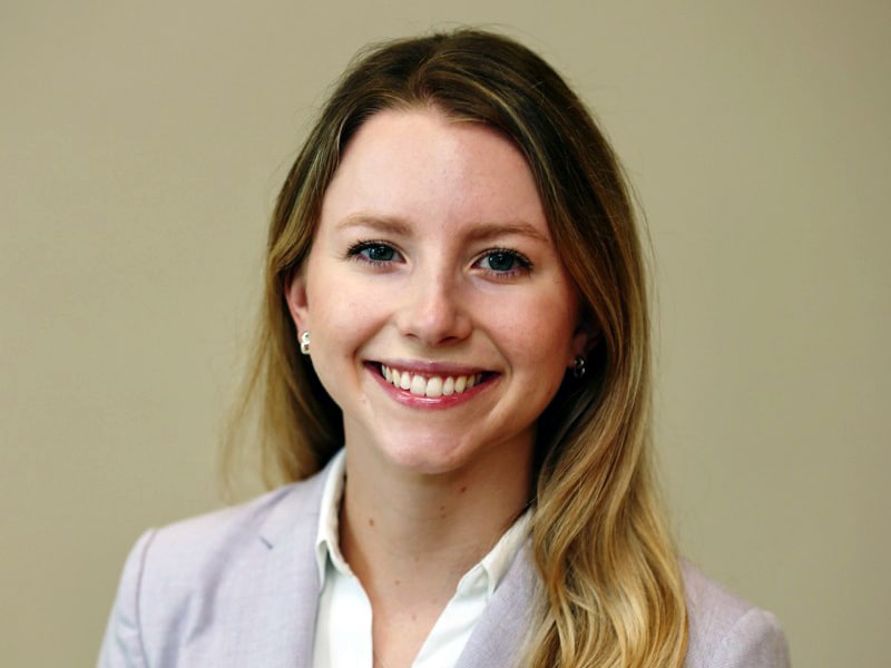 A young woman with long blonde hair smiles confidently at the camera while wearing a light purple blazer and white blouse. She has a professional, polished look.