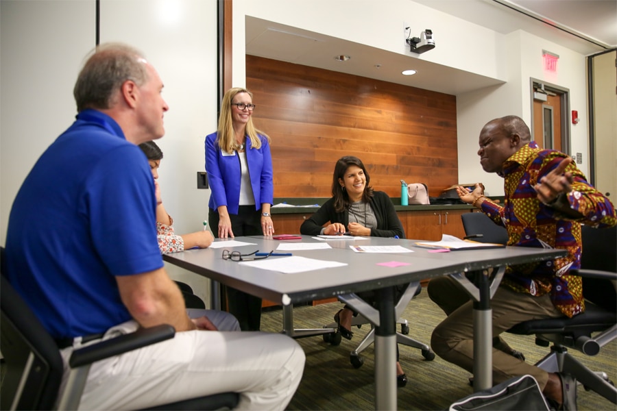 A diverse group of professionals actively participates in a group discussion during a PURC training course, seated around a table in a classroom setting.