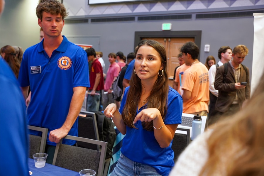 Two Warrington Diplomats in matching blue polo shirts engage with attendees at a busy career event, surrounded by students and informational booths.