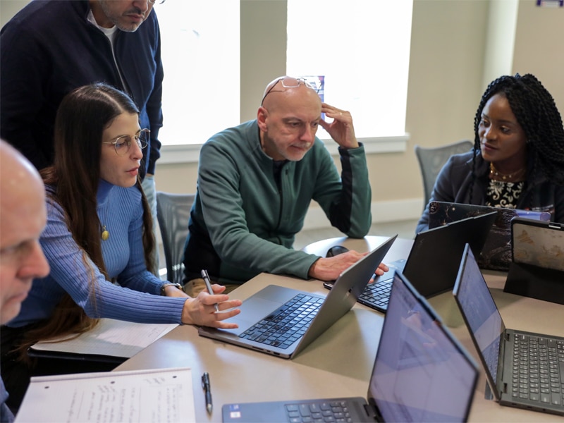 A diverse group of DBA students collaborate around a table with laptops, actively discussing ideas during an on-campus session at the University of Florida Warrington College of Business.