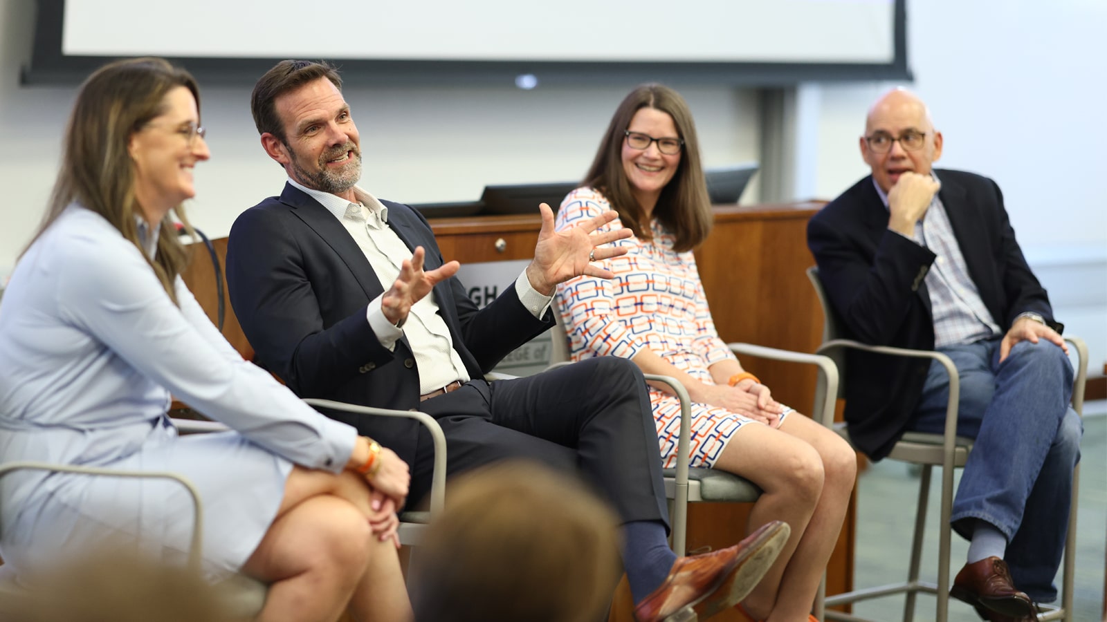 A panel of professionals discusses financial technology and its impact on business during a session at the Warrington College of Business, with engaged students listening in the background.