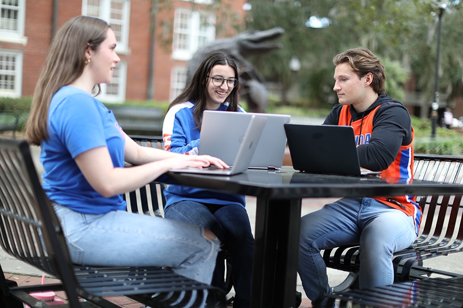 Students using laptops on campus in Gator apparel. 