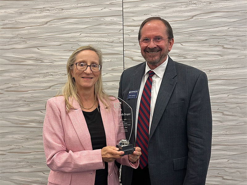 A man in a suit presents the Gerald L. Gunter Distinguished Service Award plaque to another man in a suit at the PURC Annual Conference, with lush greenery in the background.