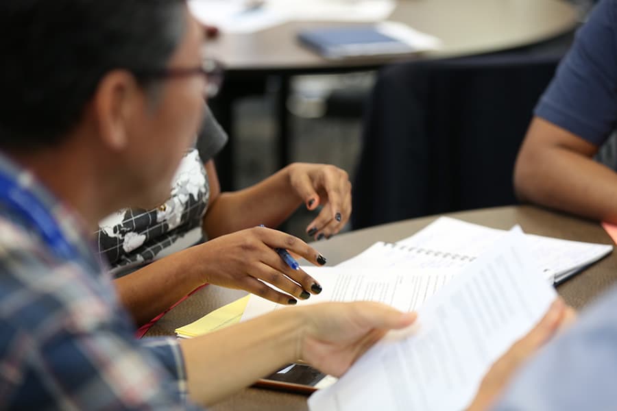 Closeup of multiple people at a table going through papers.