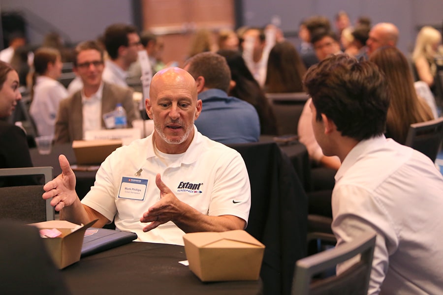 Industry professional sitting at a table speaking with a student at a career event.