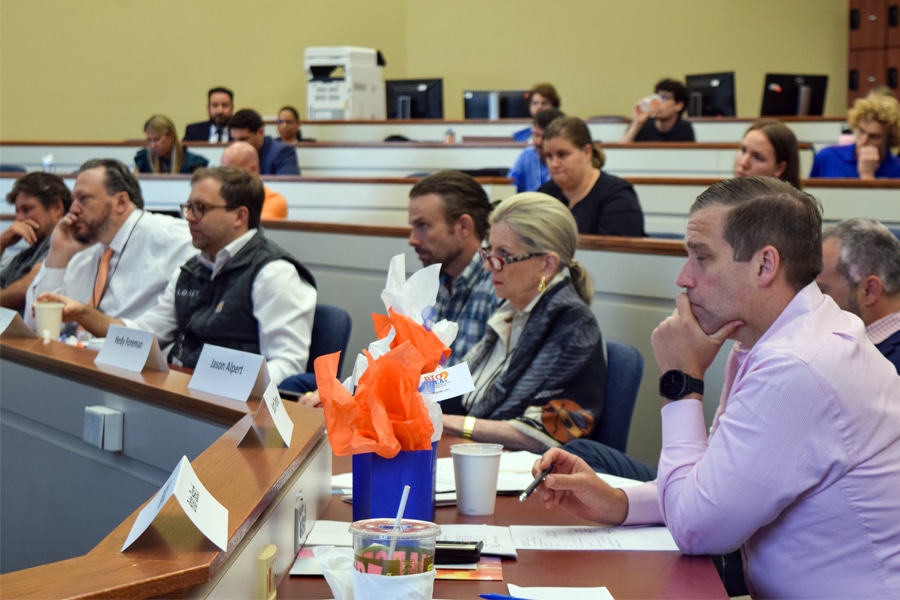 A panel of judges seated in a lecture hall, intently reviewing documents and evaluating student business plans during the preliminary judging phase.