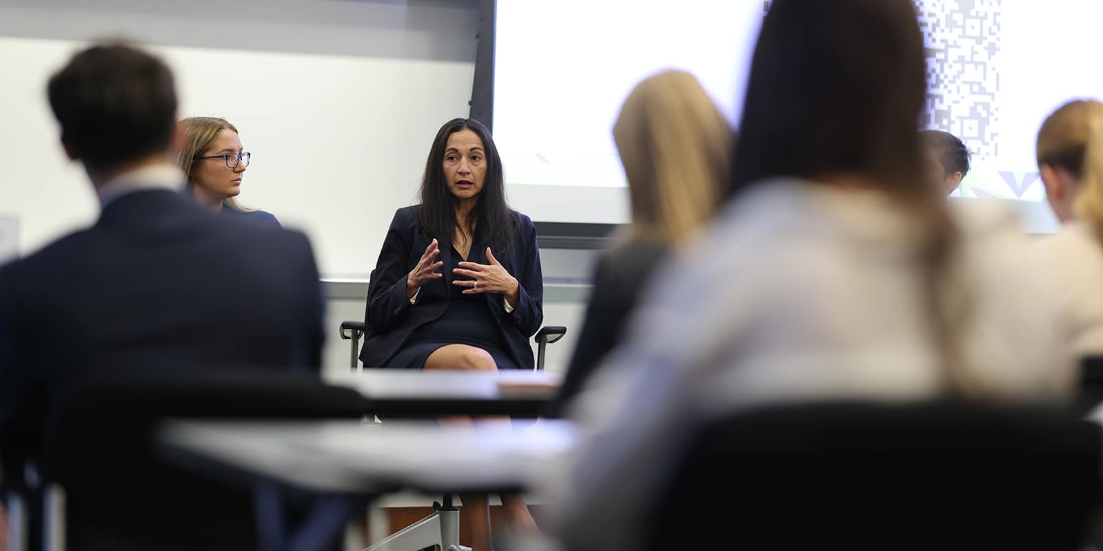 Sitting in a chair, one of Warrington's partners speaks to a classroom of MS in Business Analytics students