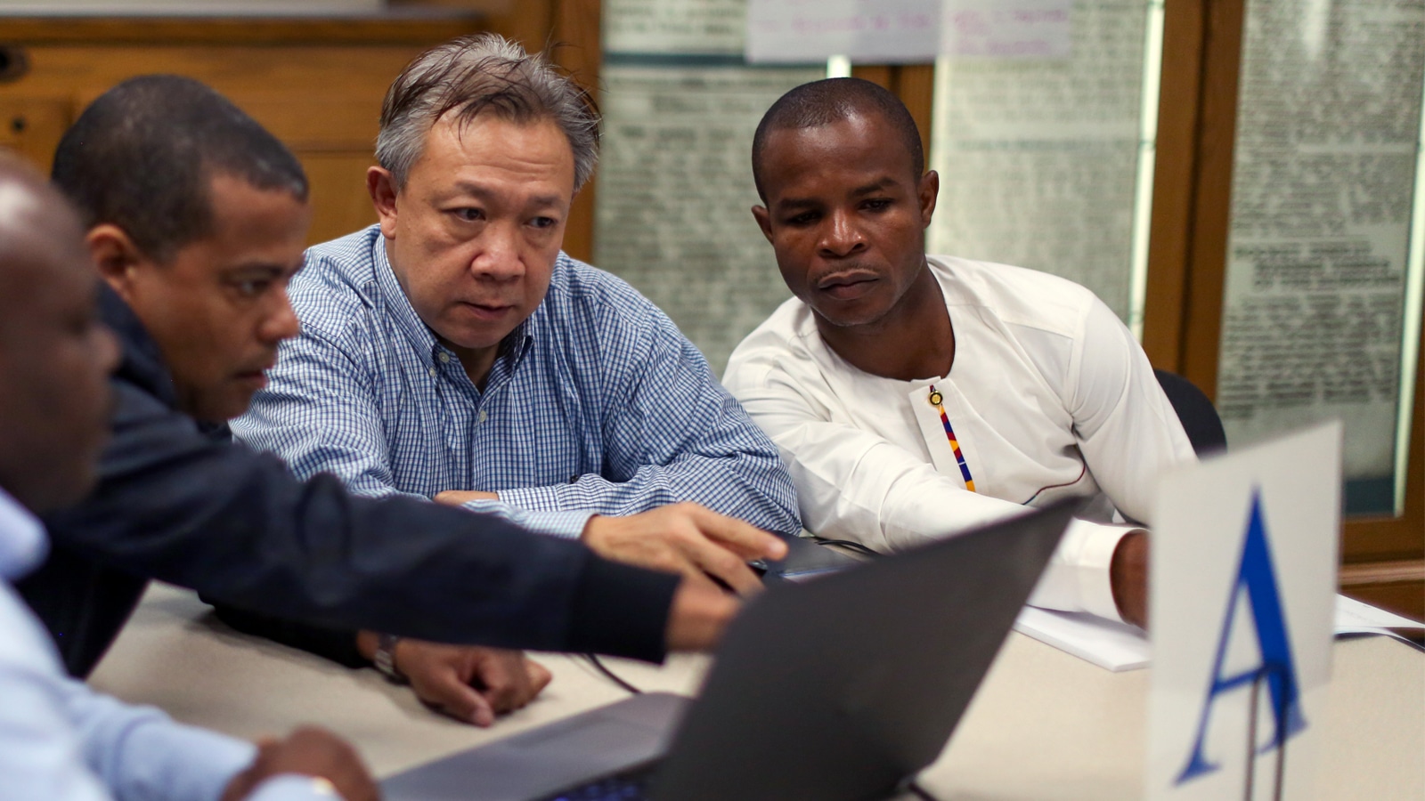 A group of men in professional attire collaborate intently over a laptop at a workshop hosted by the Public Utility Research Center (PURC).