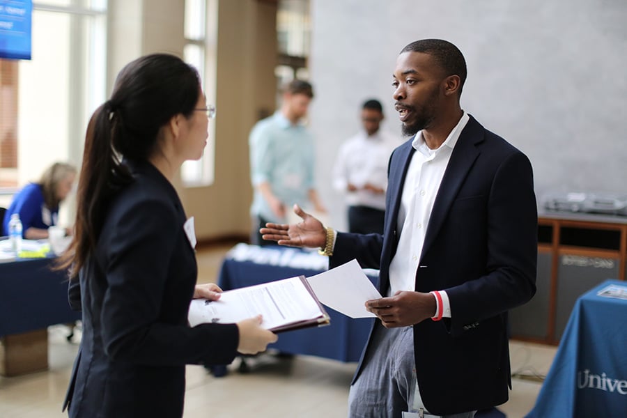 A businessman talking with a businesswoman at a recruiting event.