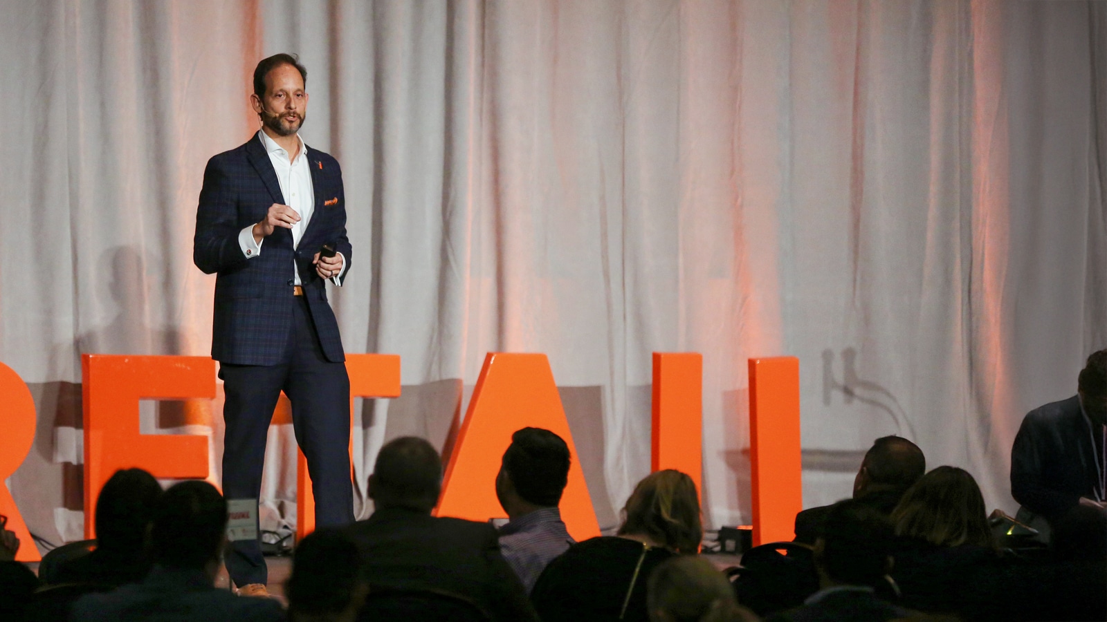 Alex Savilla stands on stage at the Retail Smarter Conference, addressing an engaged audience.