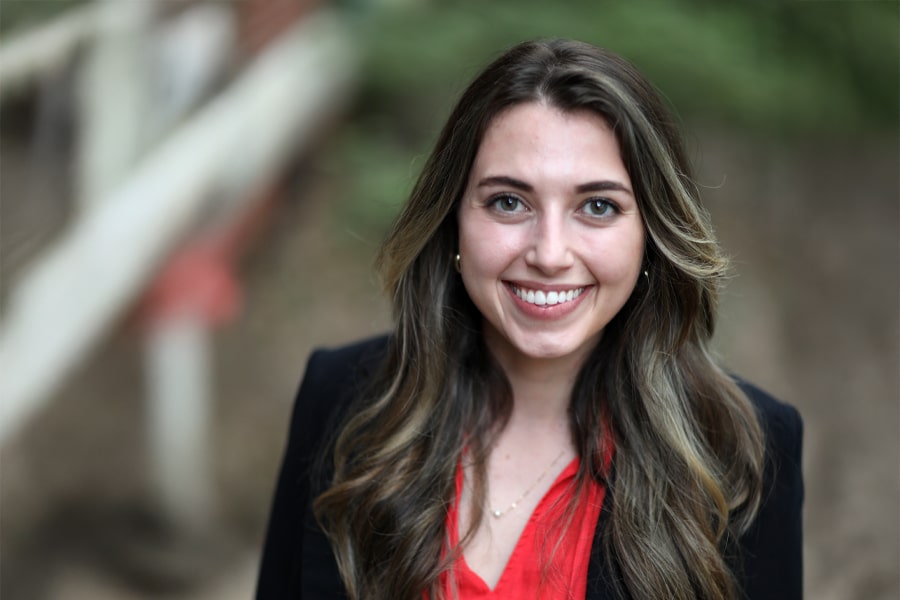 Portrait of Sofia Pérez Arrubla, a young woman with long hair wearing a black blazer and red blouse, smiling outdoors with a blurred natural background.