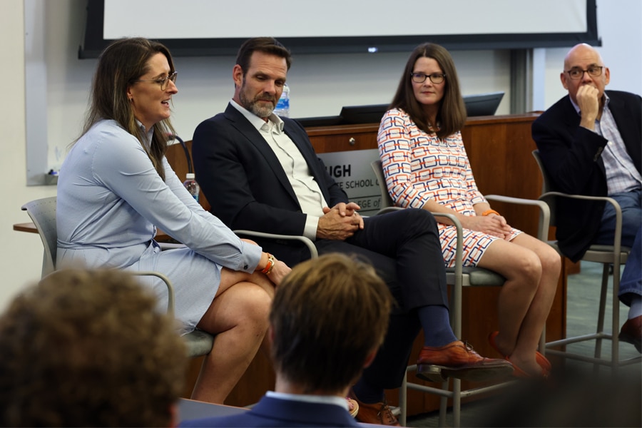 Four finance professionals sit at the front of a classroom, participating in a panel discussion during a speaker series event, with an audience listening attentively.