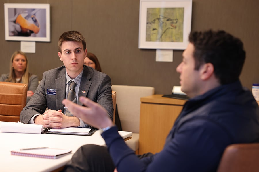 Student sitting at a table with a industry professional listening to him speak and taking notes.
