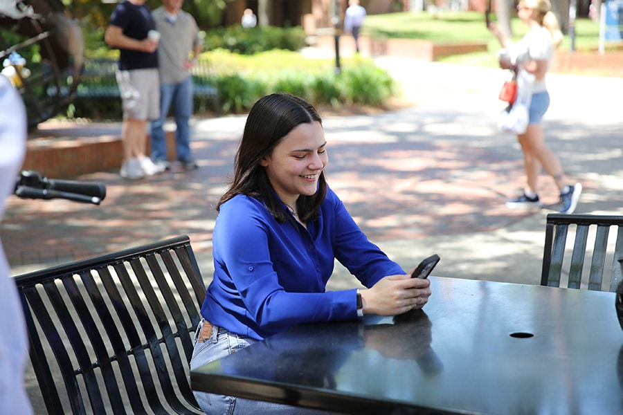 Student sitting outside smiling down at her phone.