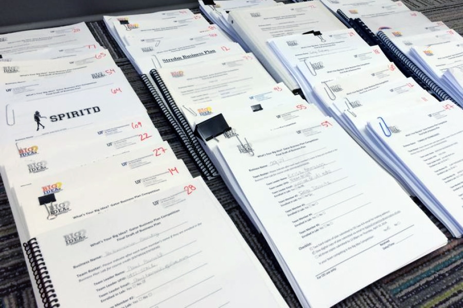 Stacks of printed and bound business plan submissions arranged on the floor, each labeled with “Big Idea” and team information.
