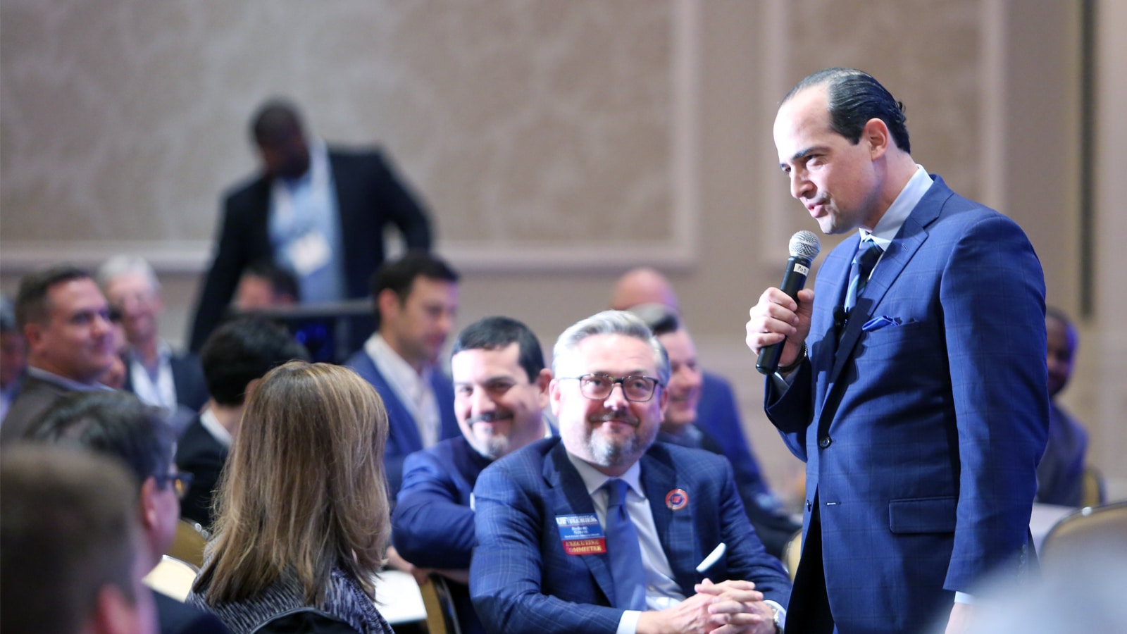 A confident man in a navy suit speaks into a microphone while engaging with attendees at the Trends Conference, hosted by the Kelley A. Bergstrom Real Estate Center.