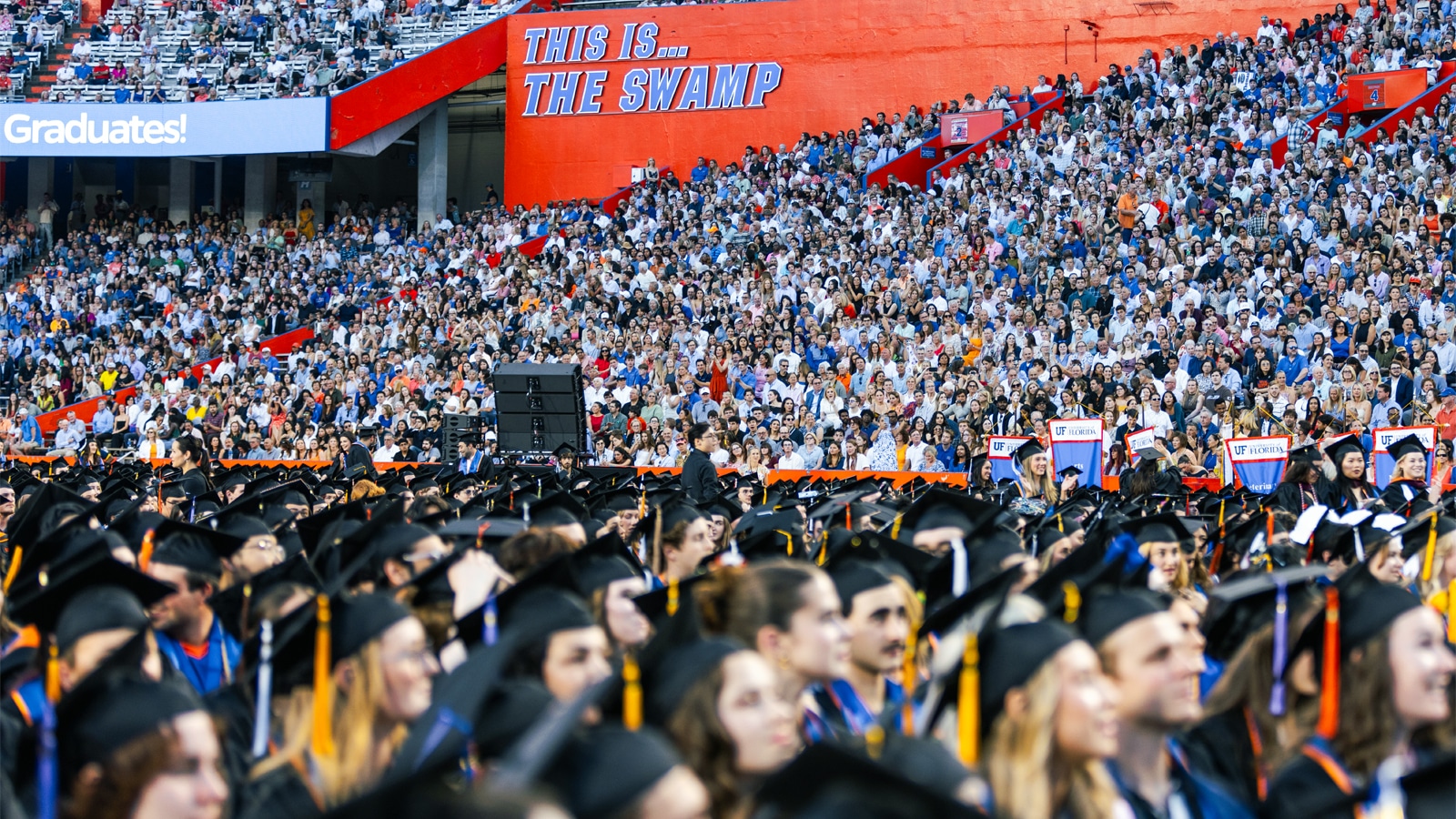 A packed stadium filled with graduates in black caps and gowns and an audience of family and friends at the University of Florida’s university-wide commencement ceremony.