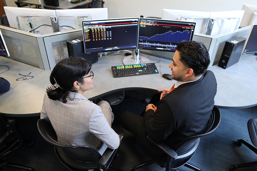 Two Warrington College of Business undergraduate students participating in Caimanes Student Managed Equity Hedge Fund review finance data on two computer monitors