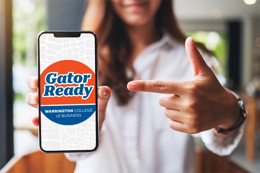 A hand points to a smartphone open to the Gator Ready app, used by the UF Warrington College of Business to track career readiness requirements
