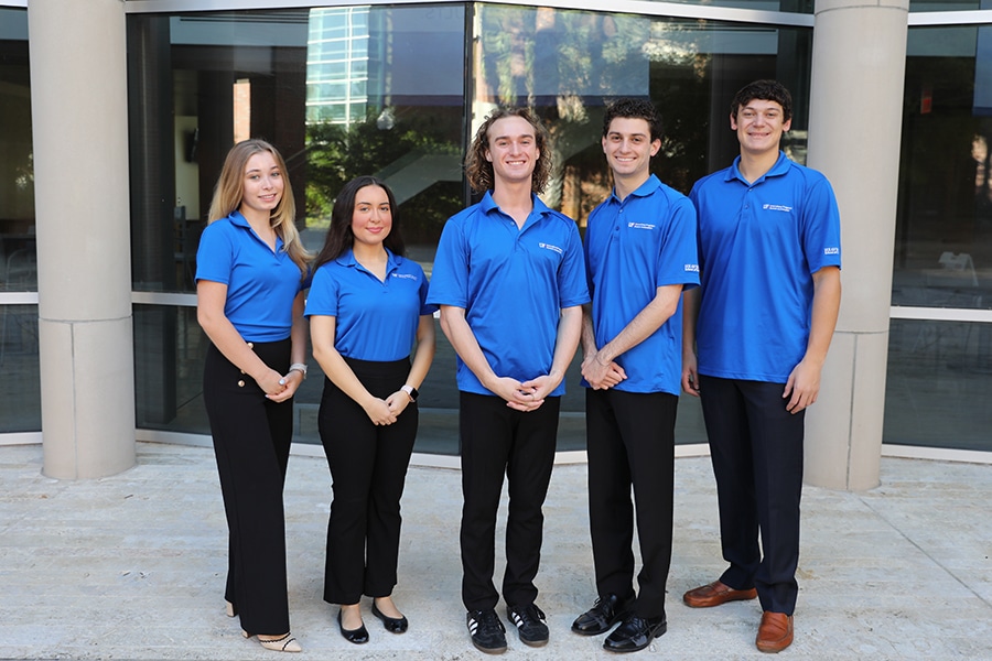 Undergraduate ambassadors for the University of Florida Warrington College of Business stand in a row in front of a building while wearing blue shirts