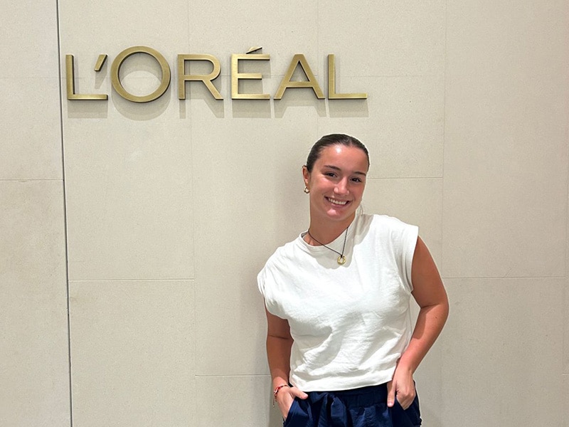 Amanda Veltri standing in front of a L'Oreal sign at her internship.