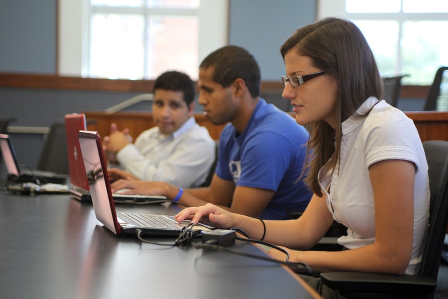 Three students work on laptops in a classroom, focused on real estate software training as part of their coursework.
