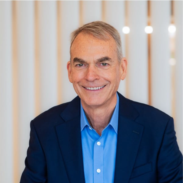 Professional headshot of Alex Smith, smiling, wearing a navy blazer and light blue dress shirt, posed in front of a vertical white-striped background.