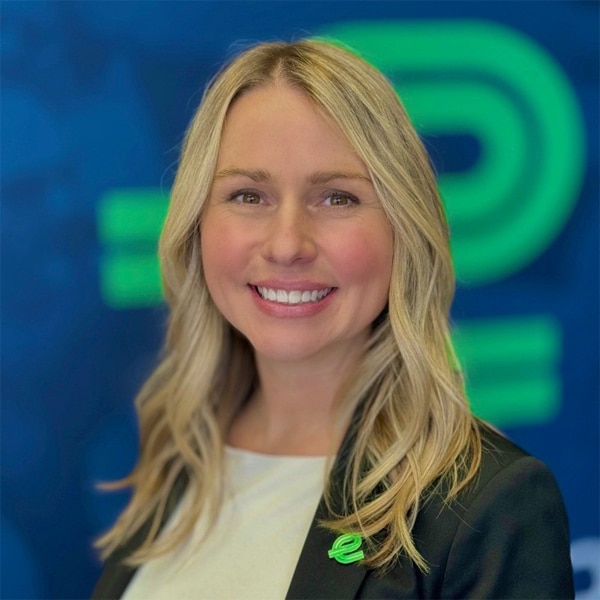 Headshot of Amy Casari, smiling, with long blonde hair, wearing a black blazer and white top, in front of a blue and green Enterprise Mobility backdrop.