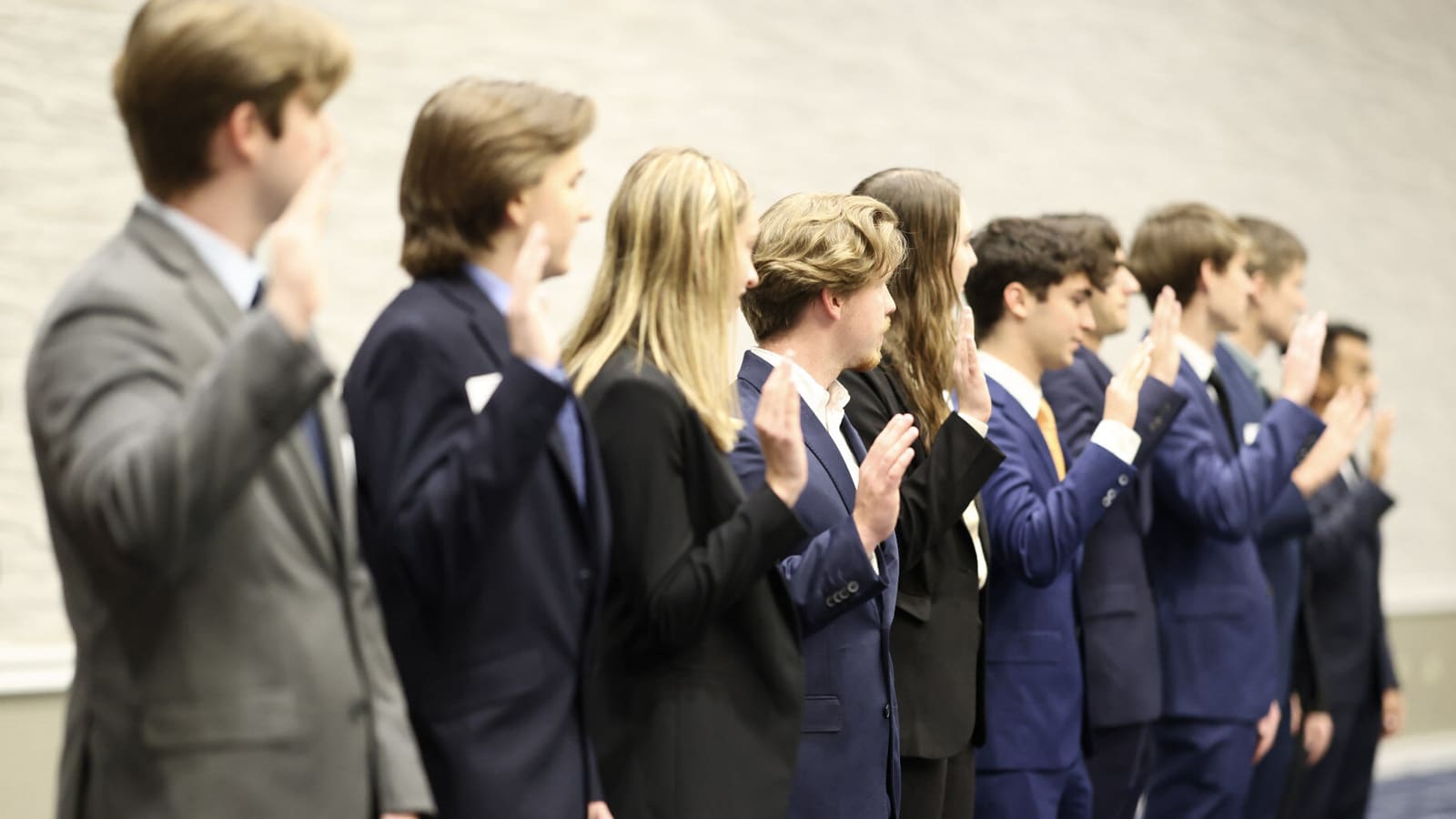 Students in business attire raise their right hands during an induction ceremony