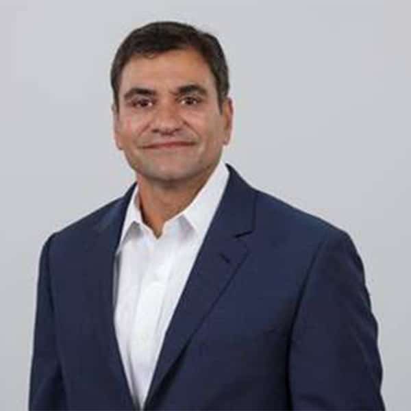 Professional headshot of Chirag Bhavsar, a man with short black hair and medium complexion, wearing a navy blazer over a white dress shirt, smiling slightly, posed against a plain light gray background.