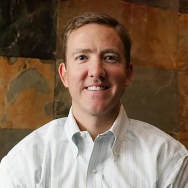 Portrait of Brian Ray, CEO of Garden of Life, wearing a light striped button-down shirt, smiling in front of a multicolored stone tile wall.