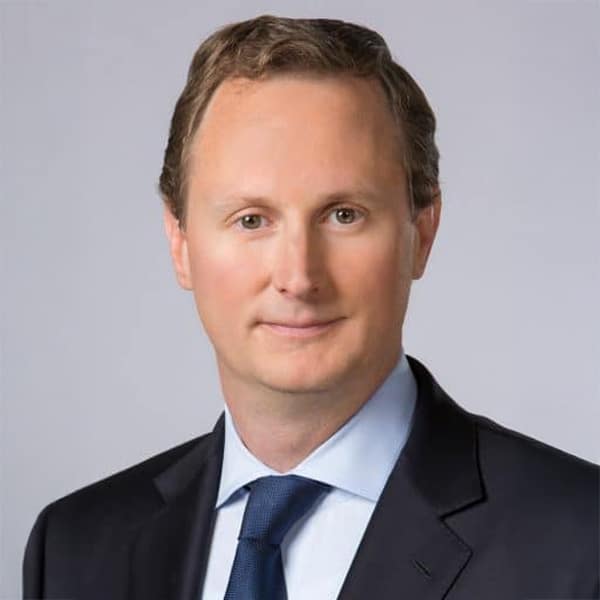 Professional headshot of Chris Winfrey, wearing a dark suit, light blue dress shirt, and navy tie, posed against a light gray background.