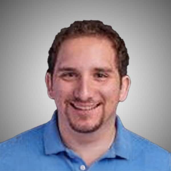 Headshot of David Magnotta, smiling, with short curly brown hair and a trimmed goatee, wearing a light blue polo shirt, in front of a gray gradient background.