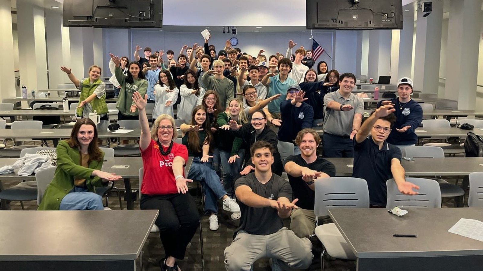 Large group of accounting students in a classroom smiling and posing with arms outstretched