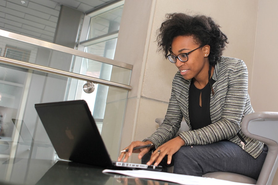Graduate student working at a table on her computer with notes beside it.