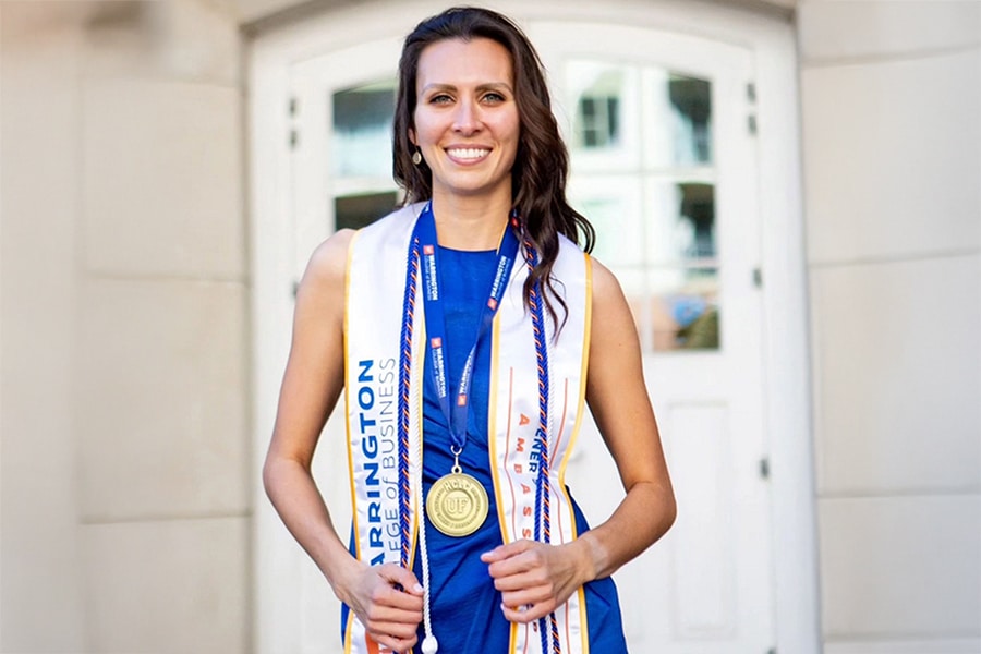 A female student wearing a Warrington College of Business graduation stole and a Heavener Career & Leadership Challenge medallion.