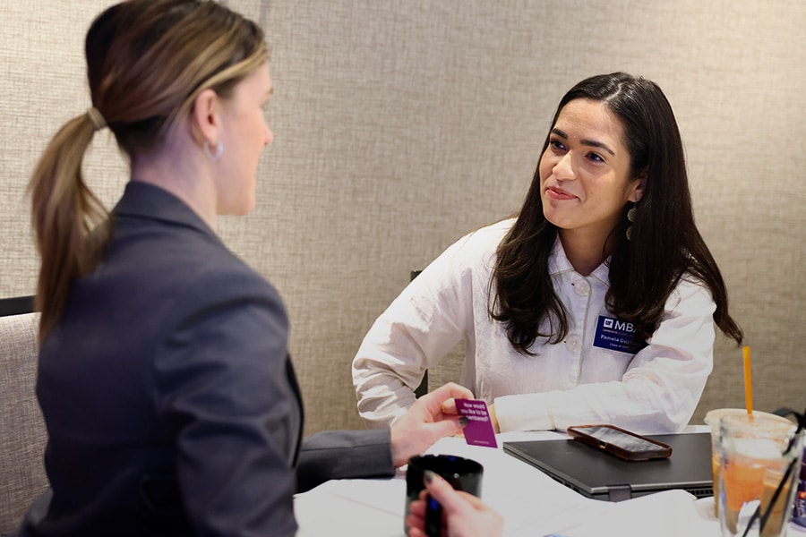 An MBA Ambassador sits with a young woman in business attire at a table.