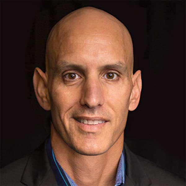 Portrait of Bill Muir, Business Advisory Council member, wearing a dark blazer and a blue shirt, smiling against a black background.