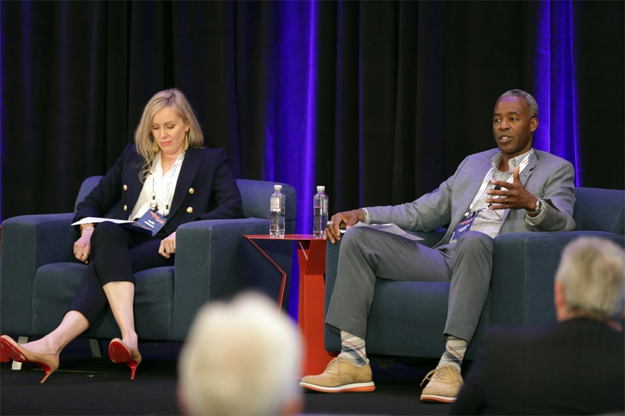 Two business professionals speak onstage during a panel discussion at a research conference