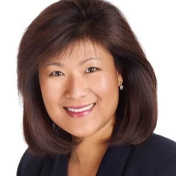 Headshot of Ann Sung Ruckstuhl, smiling, with shoulder-length dark hair, wearing a dark blazer and pearl earrings, set against a white background.