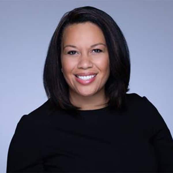 Professional headshot of Tanya Sanders, smiling, with straight shoulder-length dark hair, wearing a black top, set against a soft gray gradient background.