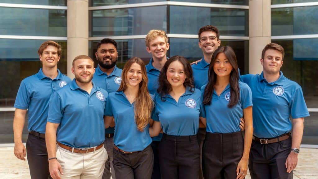 Group of UF AIS student members smiling in matching blue polos outside a business building