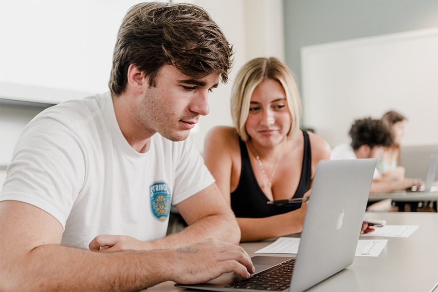 Two students look at a laptop computer in class.