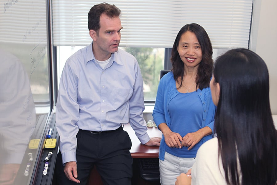PhD students and a professor standing around a white board in their office.
