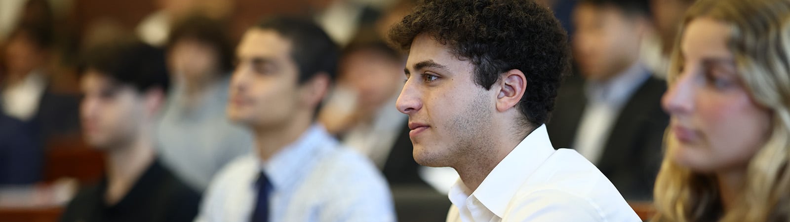 Close up photo of a student sitting in class with other students blurred in the background.