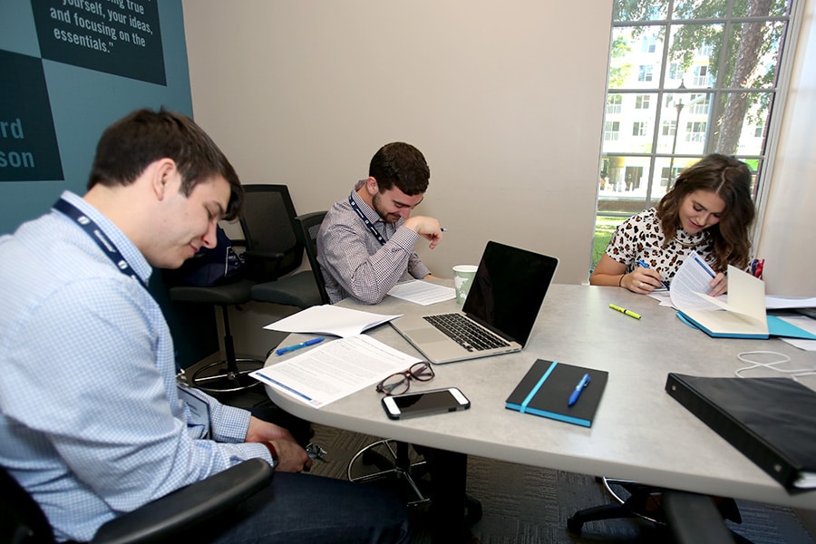 Group of students studying at a table together with their laptops and notes.