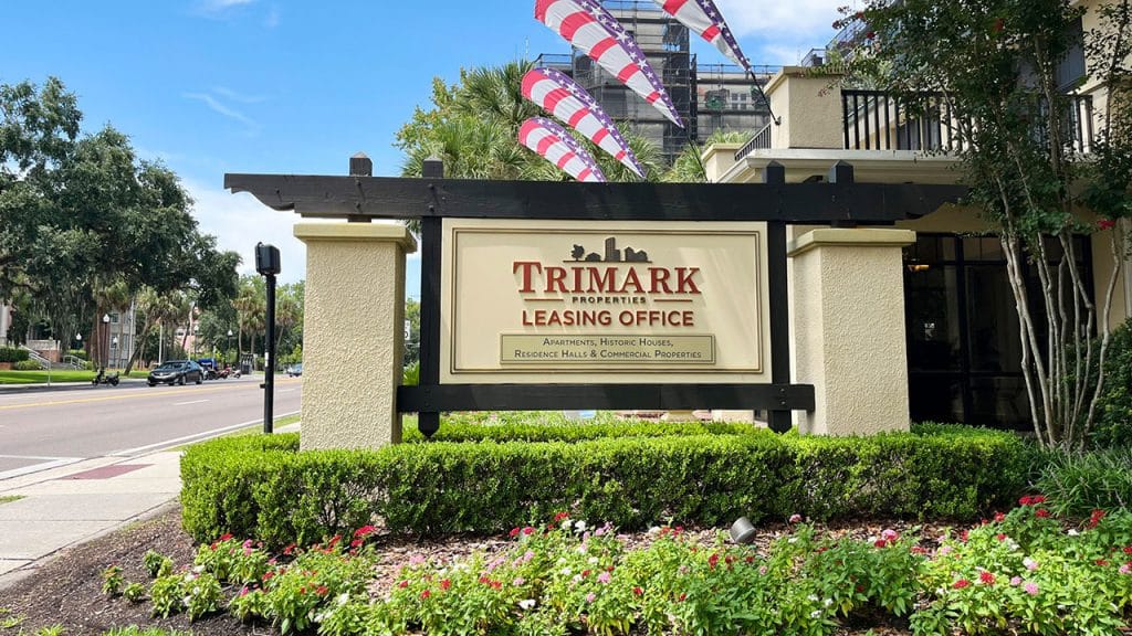 Trimark Properties Leasing Office sign outside their building with flowers and other landscaping and the street in the background.
