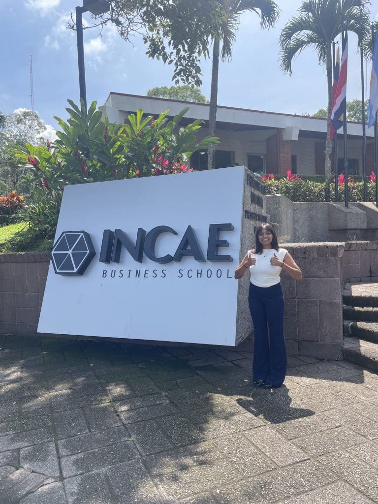 Nandini Kumar standing with her thumbs up in front of the INCAE Business School sign