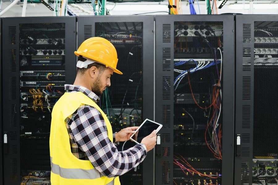 Young technician man working with tablet inside big data center room - Focus on right hand holding tablet.