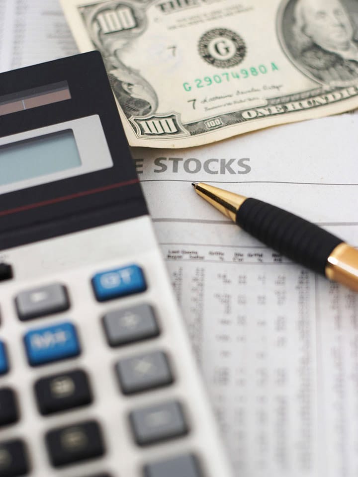 Calculator, pen, and a $100 bill on a stocks paper